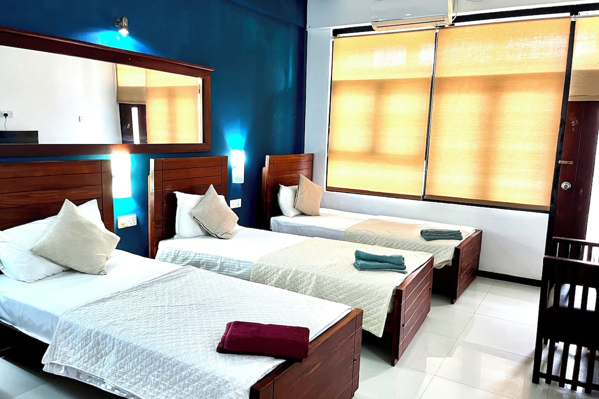A hotel room with two beds, a large window with curtains, a wooden headboard, and a desk with a chair.
