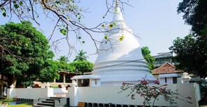 A white stupa surrounded by greenery and a small building with a tiled roof. - Subhas Hotel (Jaffna)