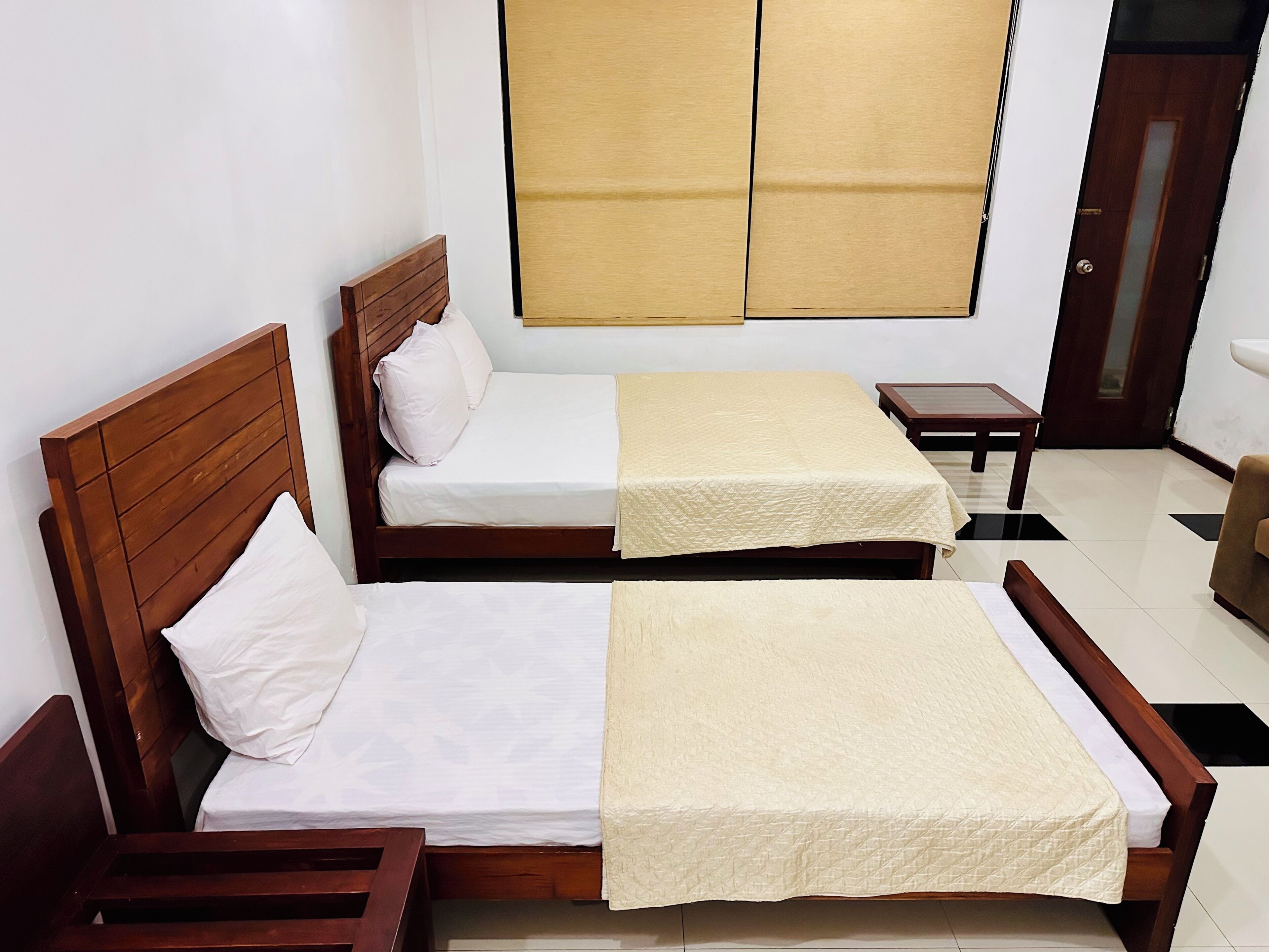 A room with two wooden beds, a small table, and a chair.