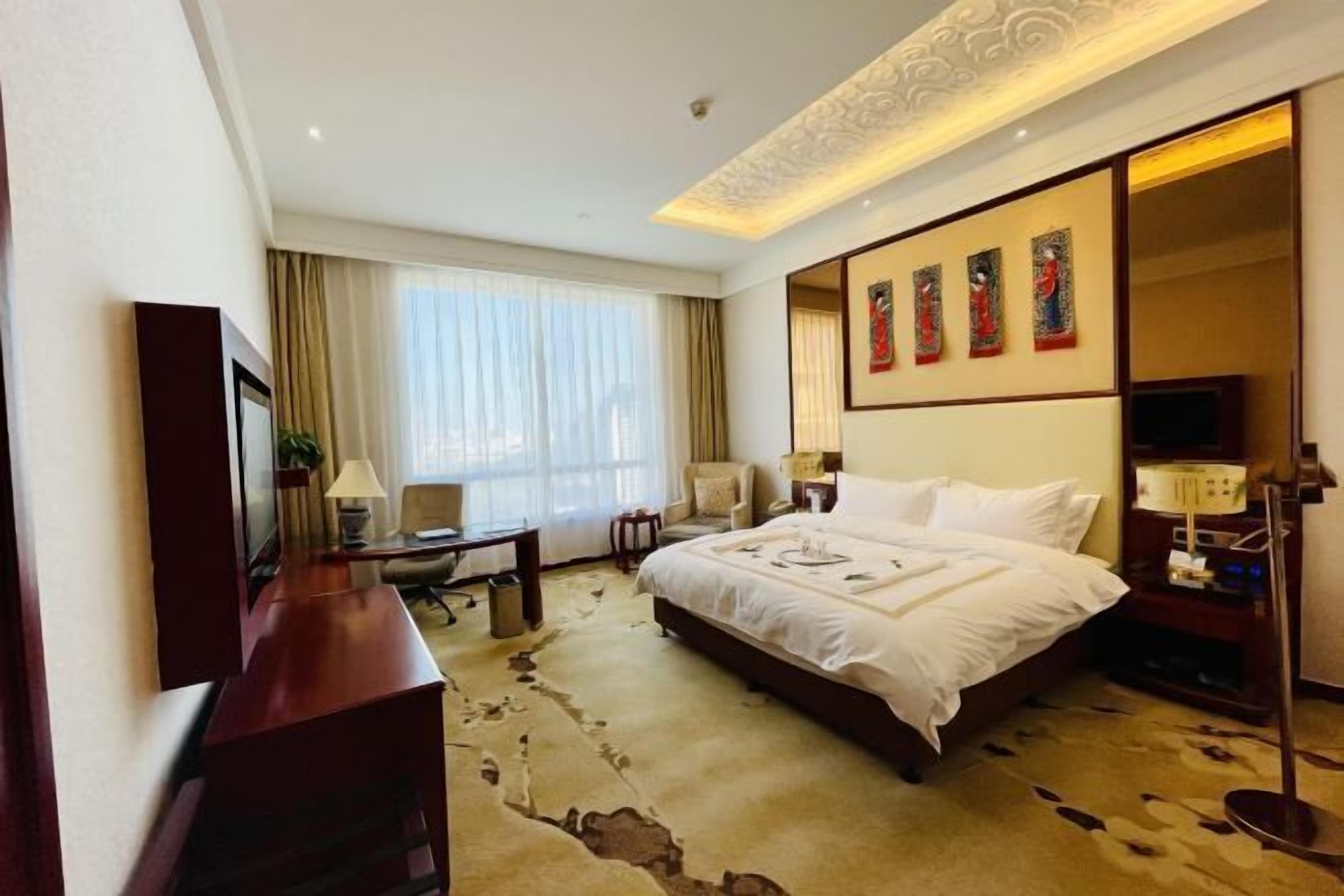 Une chambre d’hôtel avec un grand lit, un bureau, une chaise, une télévision et des œuvres d’art accrochées au mur.
