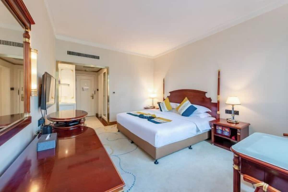 Ein Hotelzimmer mit Bett, Nachttischen, einem Schreibtisch, einem Spiegel und einer Tür zu einem anderen Raum.