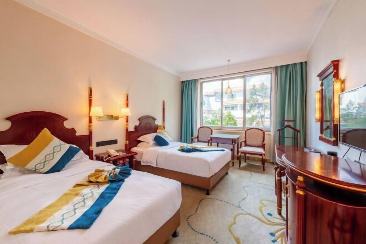 Ein Hotelzimmer mit zwei Betten, einem Schreibtisch, einem Stuhl, einem Fernseher und einem Fenster mit Vorhängen.