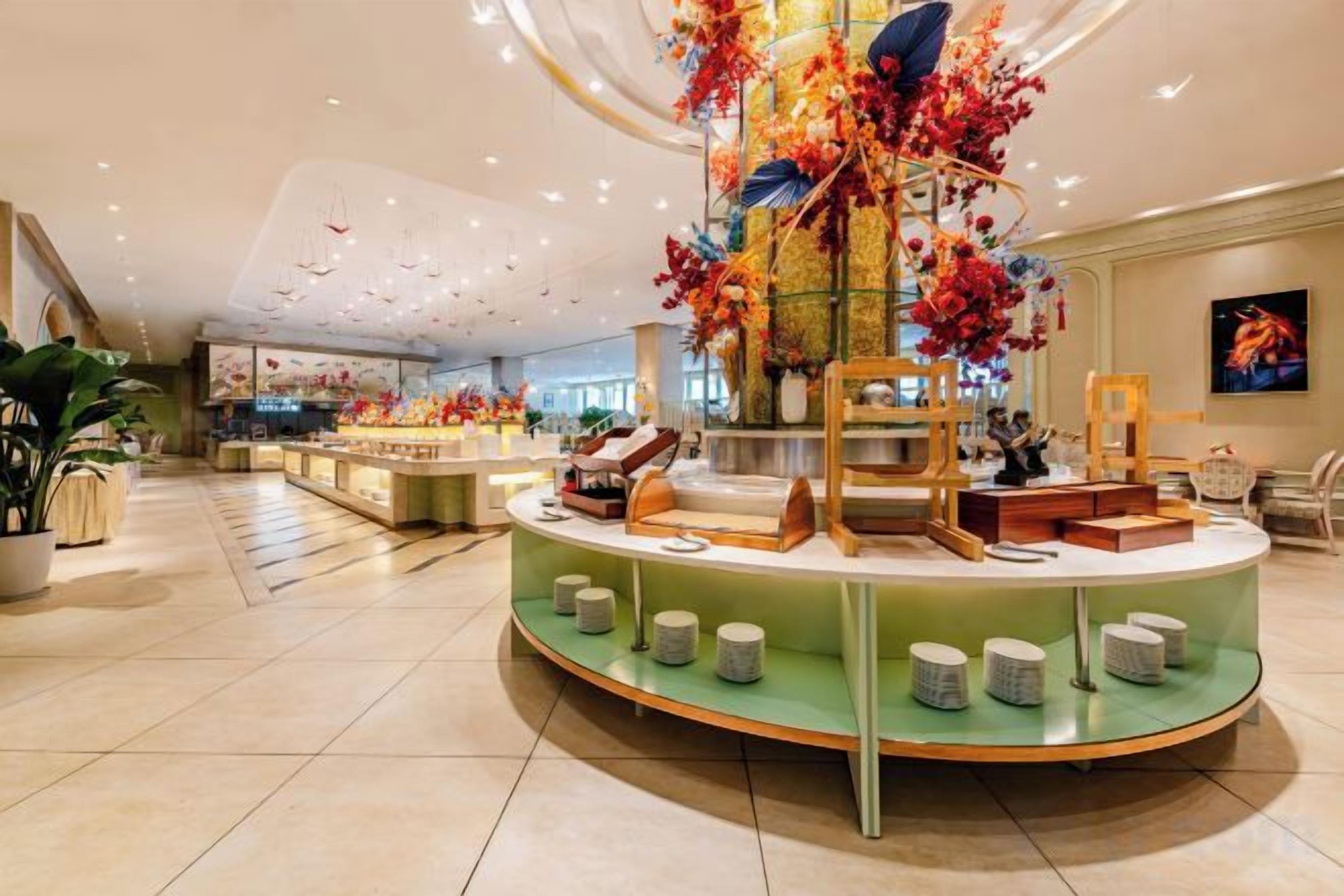 Eine Hotelhalle mit einer zentralen Rezeption, einer großen Blumenkomposition und einer Sitzecke mit Stühlen und Tischen.