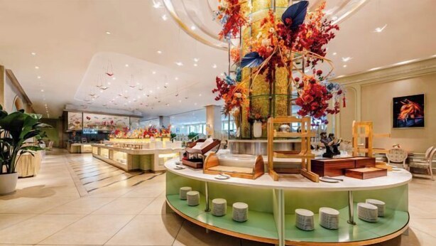 A modern hotel lobby with a central round display featuring decorative items and a seating area with cushioned stools.