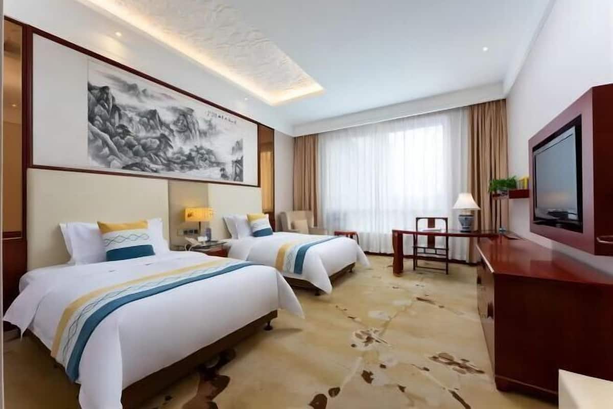 Ein Hotelzimmer mit zwei Betten, einem Schreibtisch, einem Stuhl, einem Fernseher und einem Gemälde an der Wand.