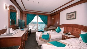 A hotel room with two beds, a desk, a chair, a television, and a view of the sea. - MS Nephtis Nile Cruise (Luxor)