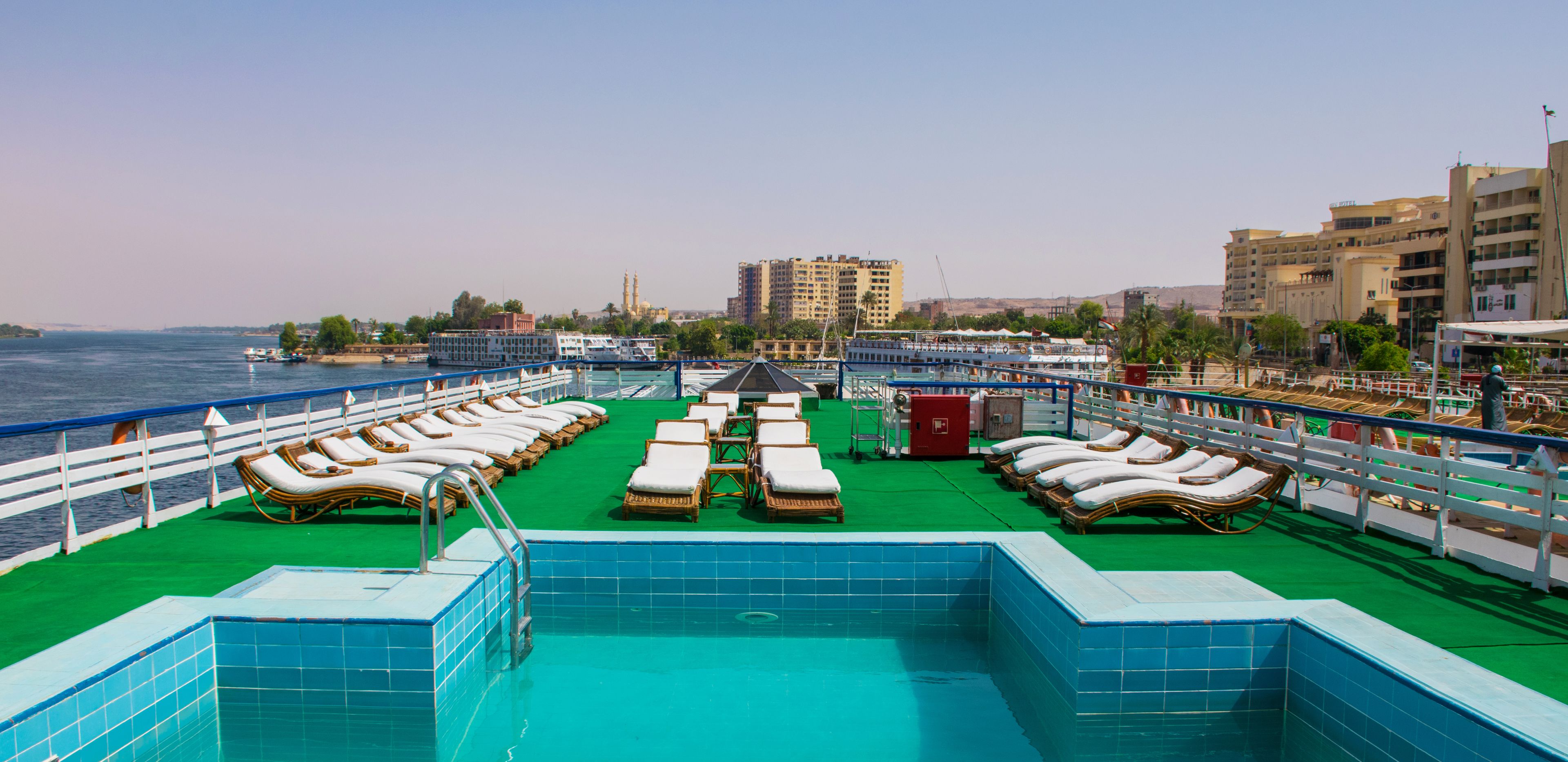 A pool area with sun loungers and a view of the sea and buildings.