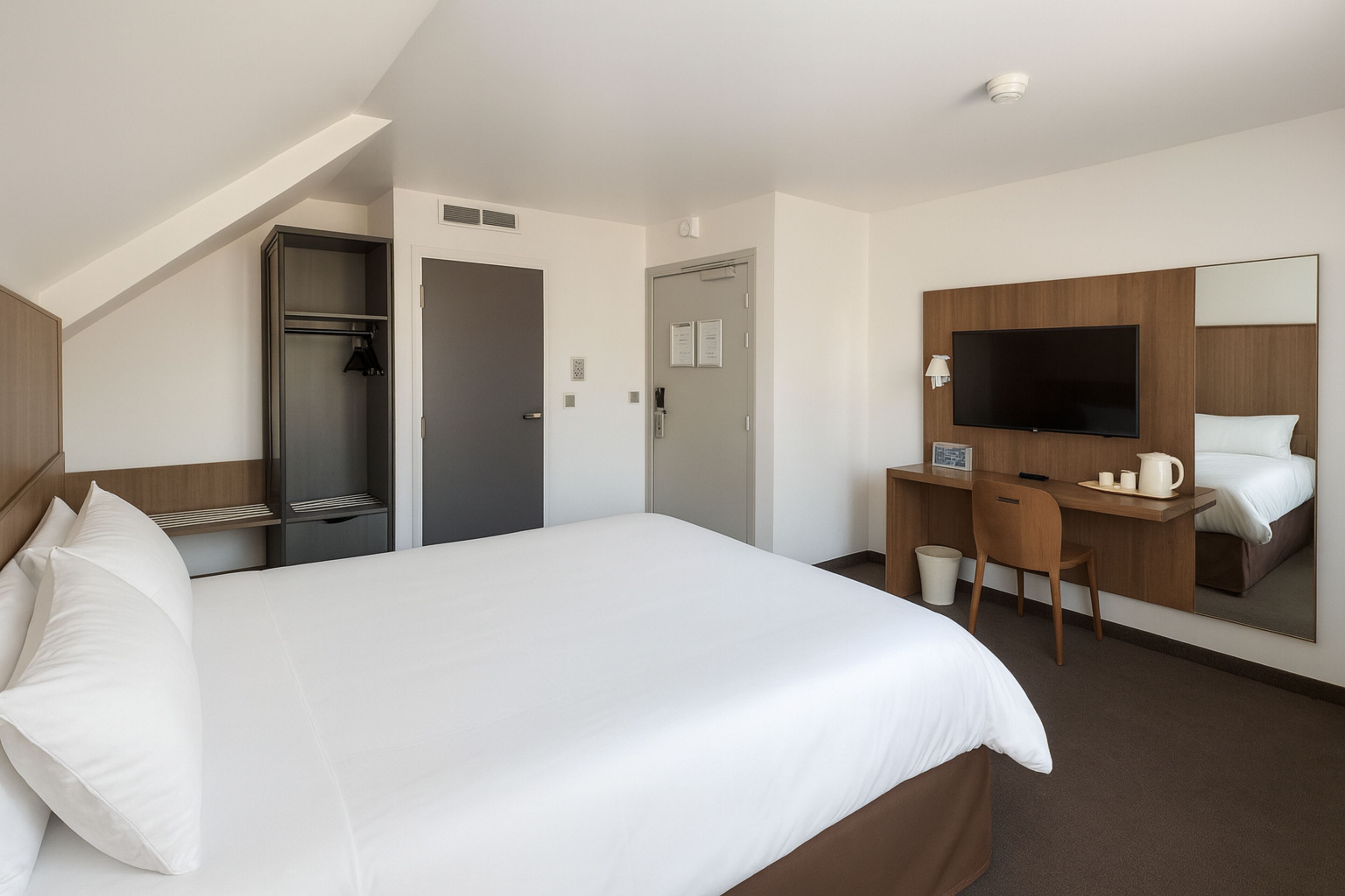 Ein Hotelzimmer mit einem großen Bett, einem Schreibtisch, einem Fernseher und einem Kleiderschrank.