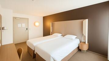 A hotel room with a bed, bedside table, lamp, and a door.