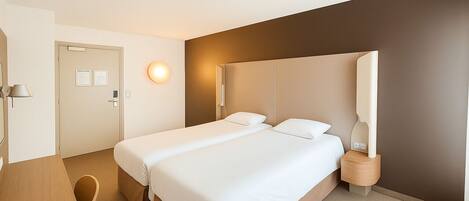 Una habitación de hotel con cama, mesita de noche, lámpara y una puerta.