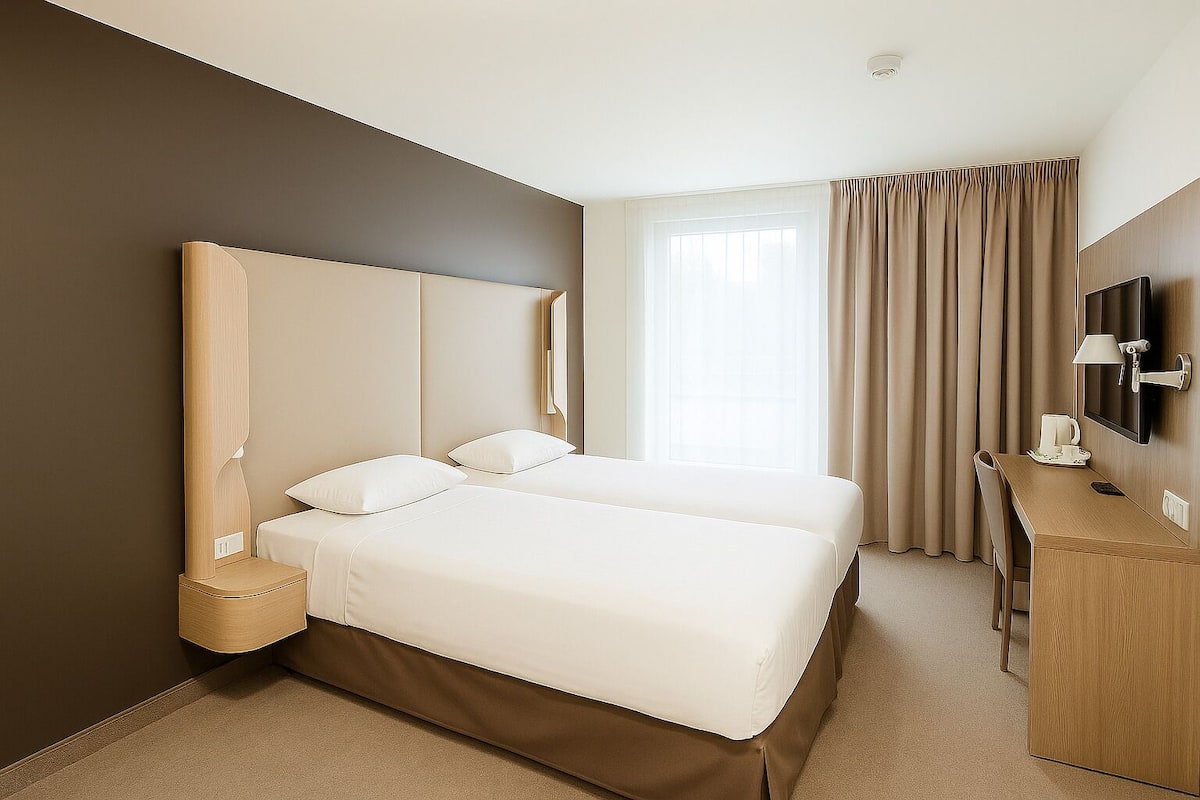 A hotel room with two beds, a desk, a TV, and a window with curtains.