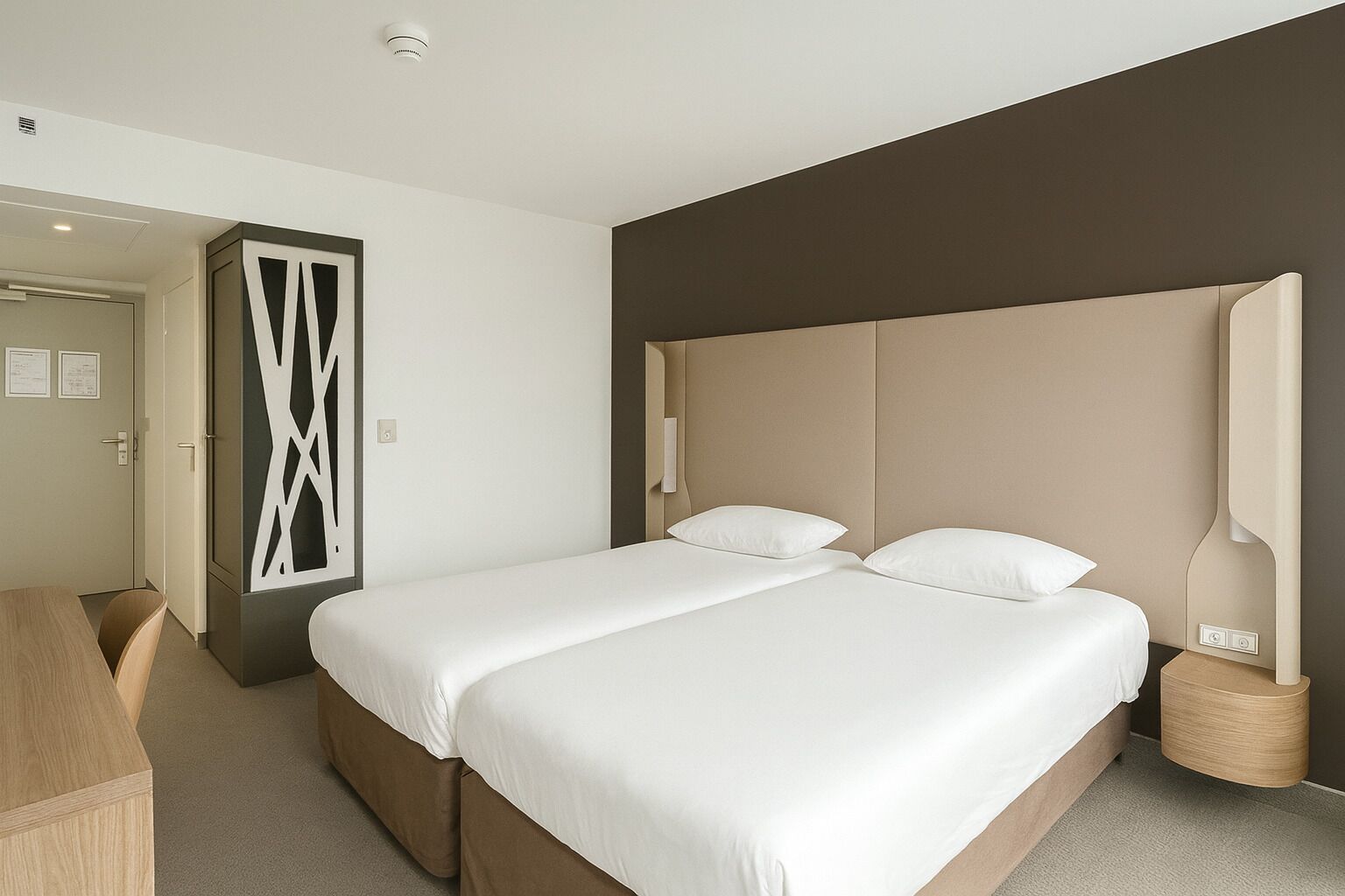 Una habitación de hotel moderna con una cama grande, un escritorio y un panel decorativo en la pared.