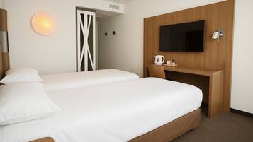 Quarto de hotel com uma cama, uma escrivaninha com televisão de tela plana, chaleira e luminária na parede.