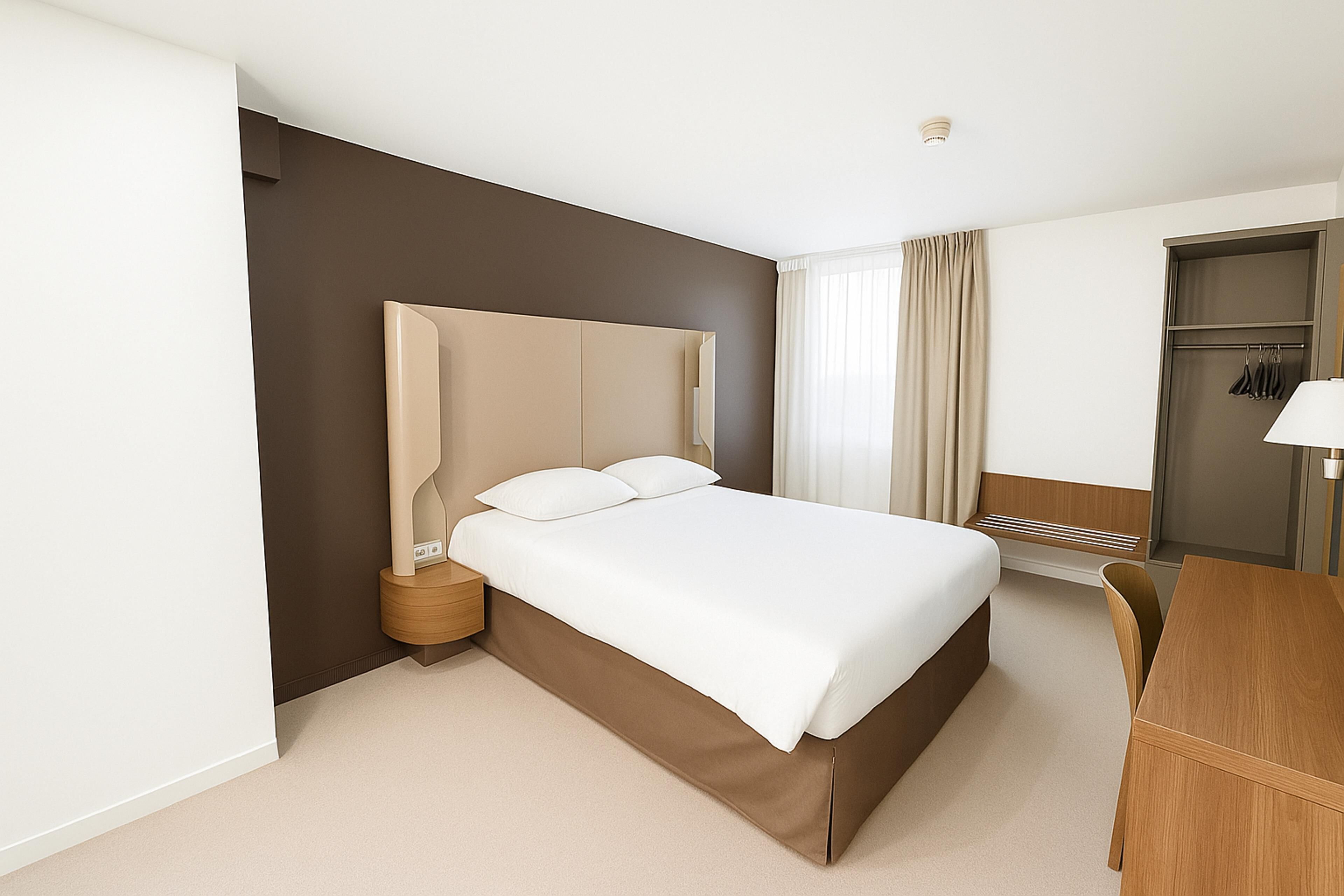 Une chambre d’hôtel moderne avec un grand lit, une table de chevet, un bureau et une armoire.