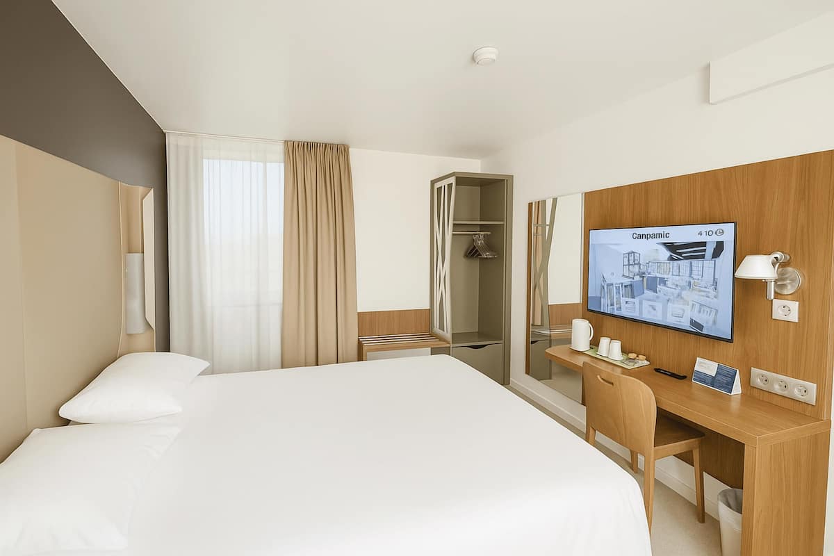 A hotel room with a bed, a desk, a TV, and a wardrobe.
