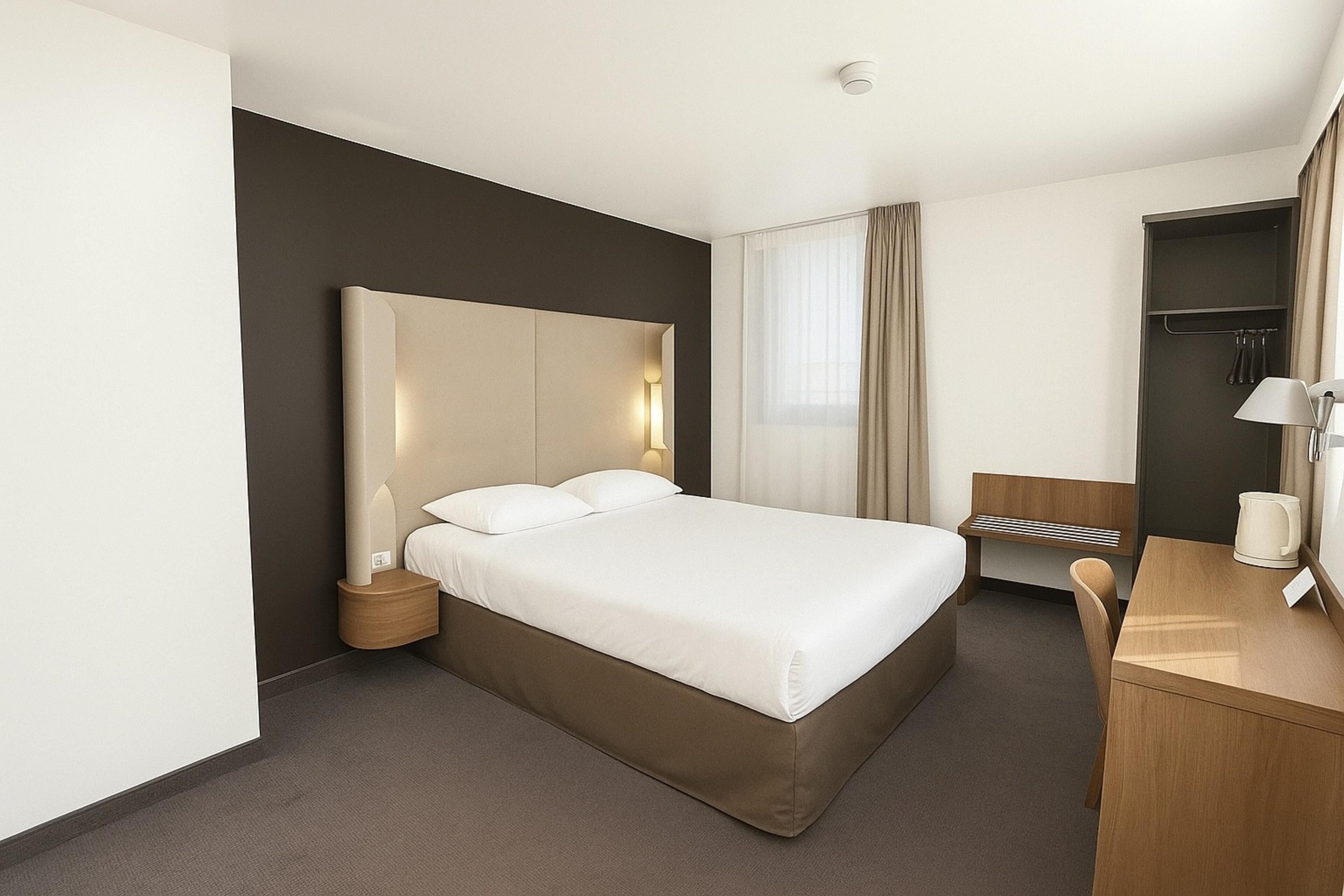 Habitación de hotel con una cama grande, mesita de noche, lámpara y escritorio con silla.