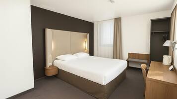 Habitación de hotel con una cama grande, mesita de noche, lámpara y escritorio con silla.