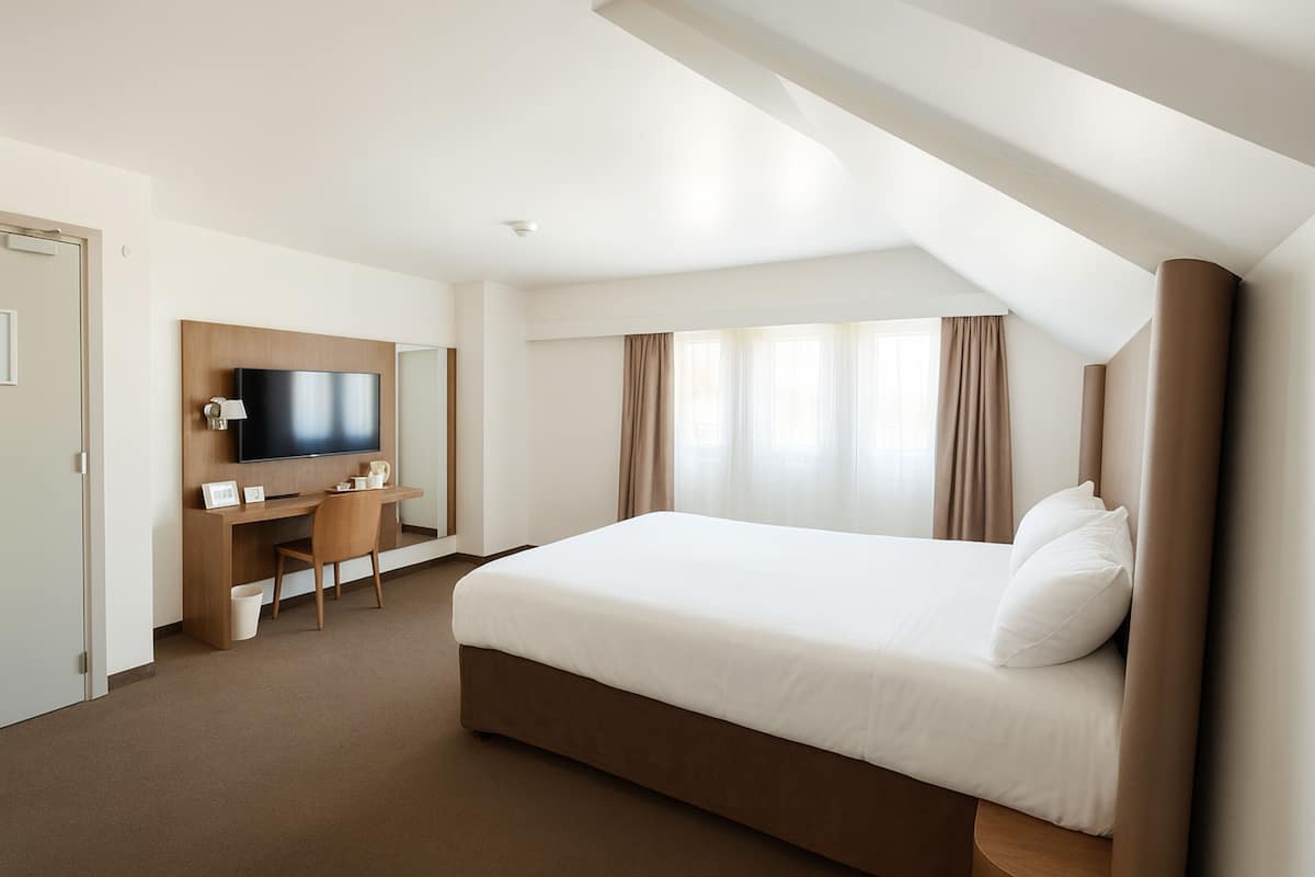 A hotel room with a bed, a desk, a chair, a television, and a window with curtains.