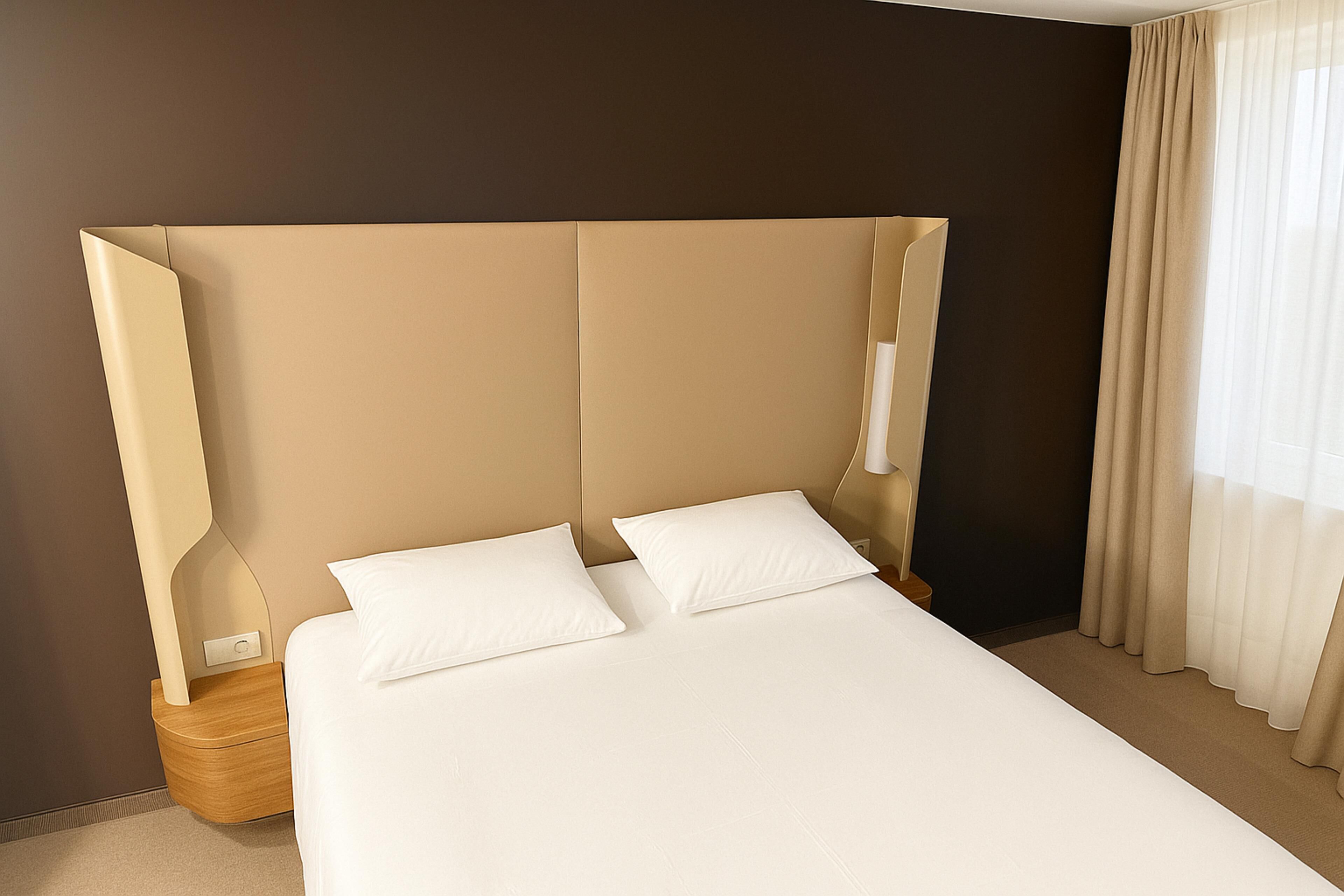 Ein modernes Hotelzimmer mit einem großen Bett, zwei Kissen, einem Nachttisch und einer Lampe.