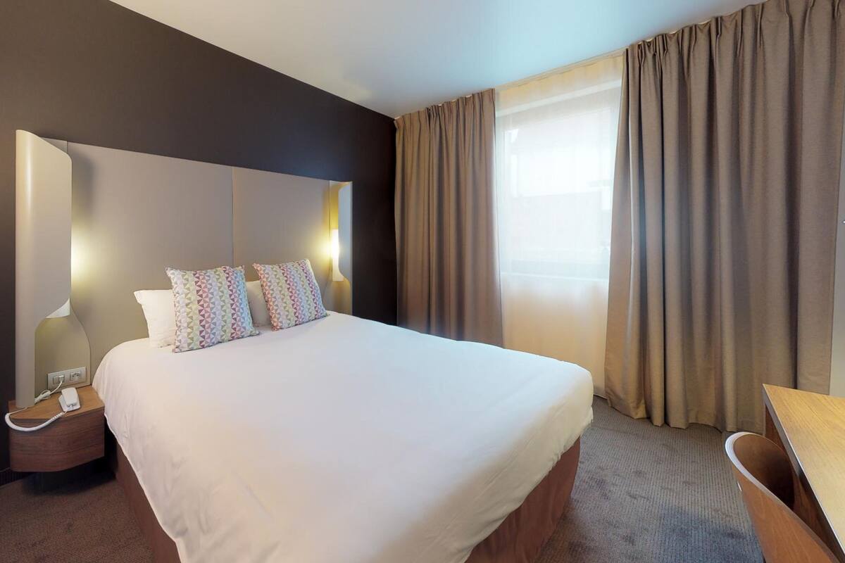 A hotel room with a large bed, bedside lamps, a telephone, and a window with curtains.