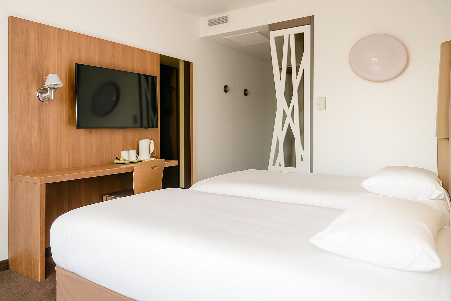 Habitación de hotel con cama, televisión instalada en un panel de madera, escritorio con silla y un adorno en la pared.