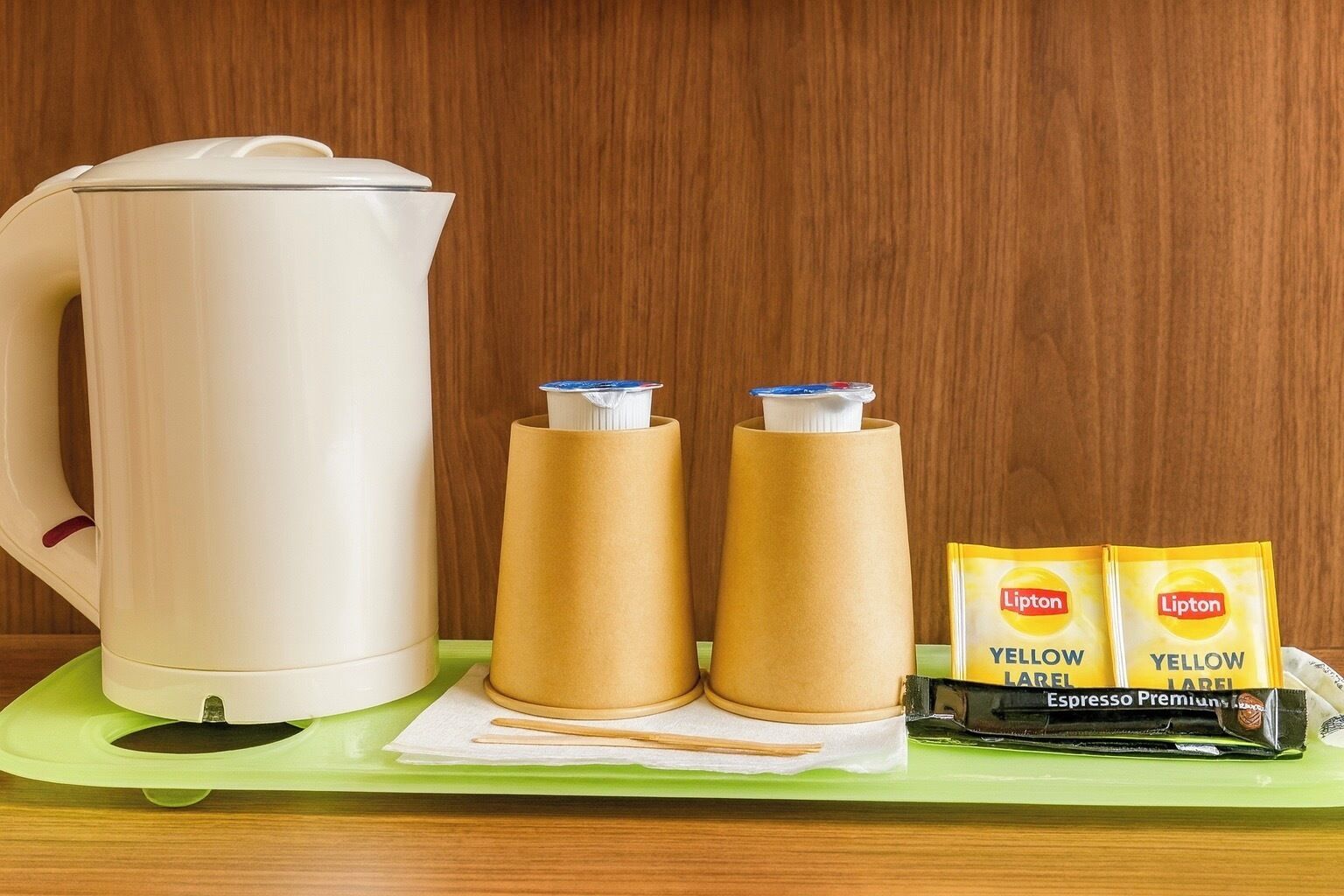 A white kettle, two brown paper cups, and two yellow Lipton tea packets on a green tray.