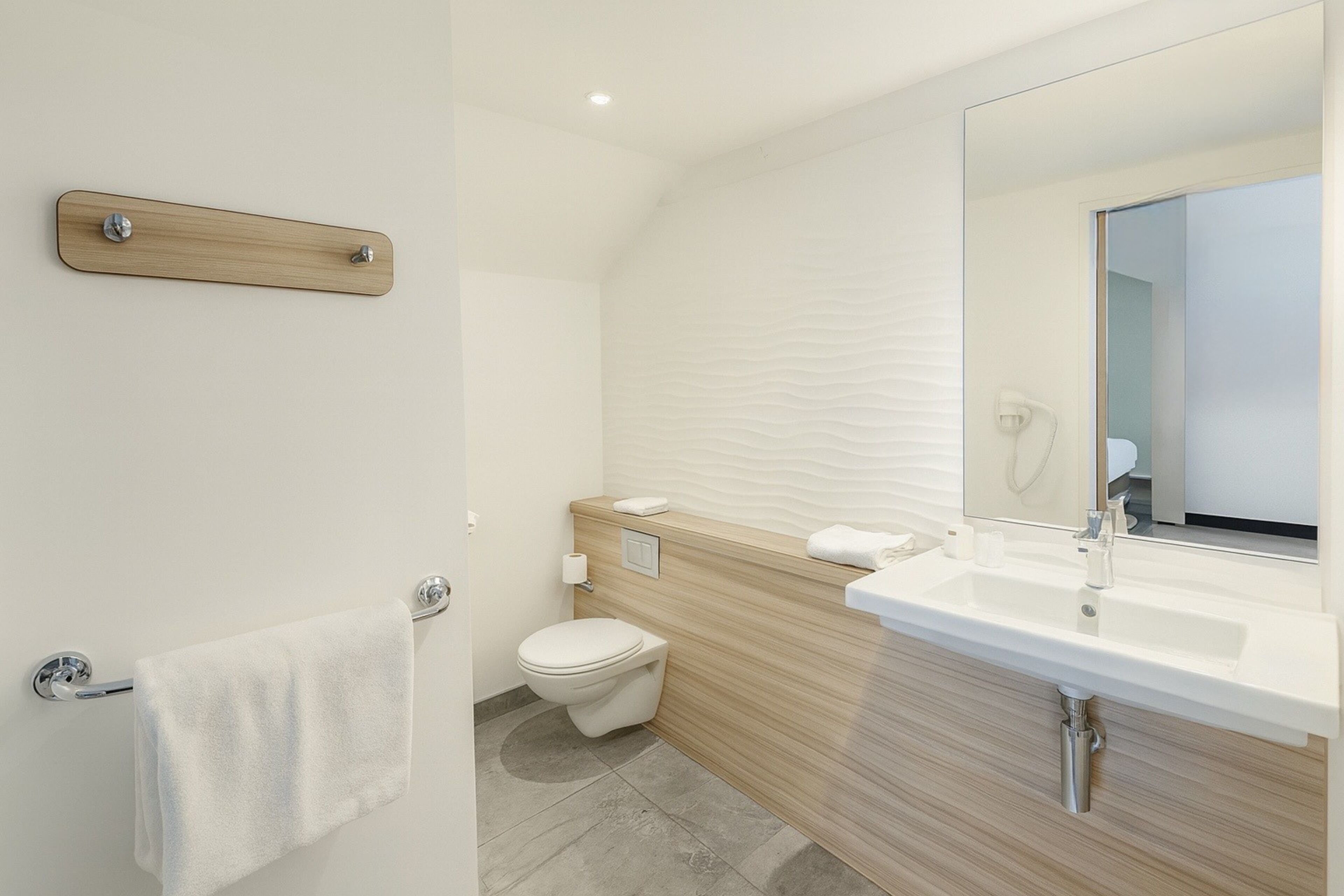 A modern bathroom with a wooden vanity, a toilet, and a towel rack.