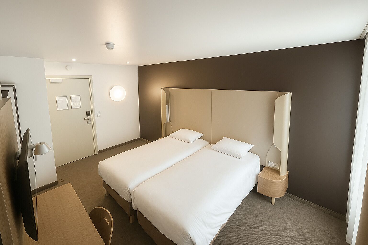 A hotel room with a double bed, bedside tables, a desk with a chair, a flat-screen TV, and a wall-mounted lamp.
