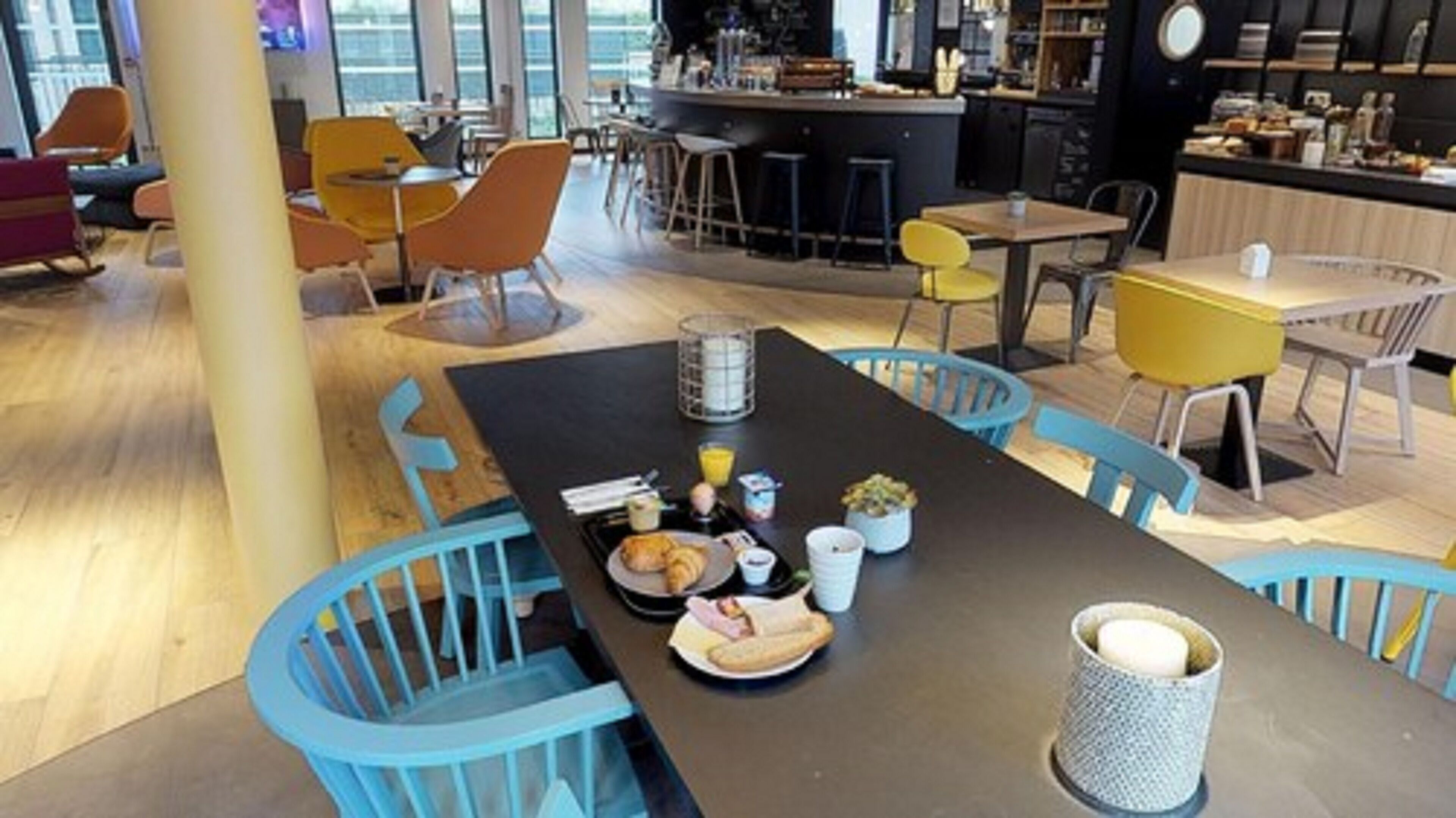 Un espace repas moderne avec une longue table, des chaises bleues et une variété d’aliments pour le petit-déjeuner.