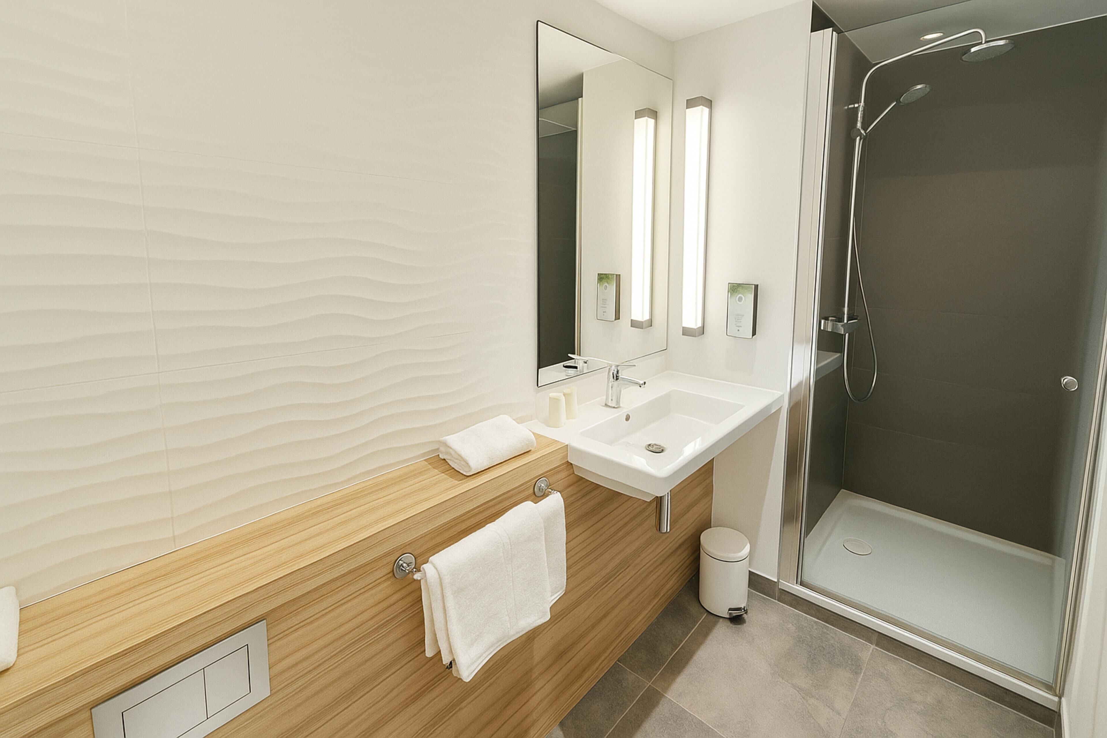 Un baño moderno con tocador de madera, dos lavamanos, un espejo grande y ducha con cerramiento de vidrio.
