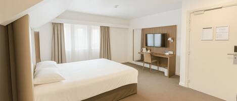 A hotel room with a bed, desk, chair, television, and a door.