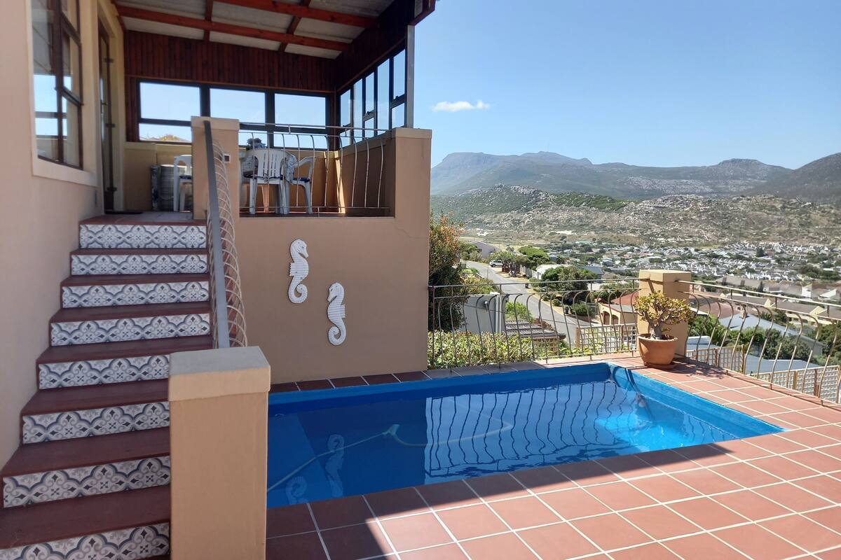 A residential property with a swimming pool, a staircase with patterned tiles, and a view of a town and mountains.