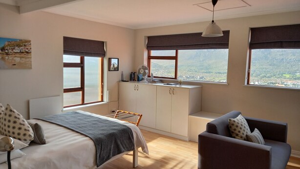 A bedroom with a bed, a desk, a chair, and a view of the landscape through large windows. - A Place in Thyme (Cape Town)