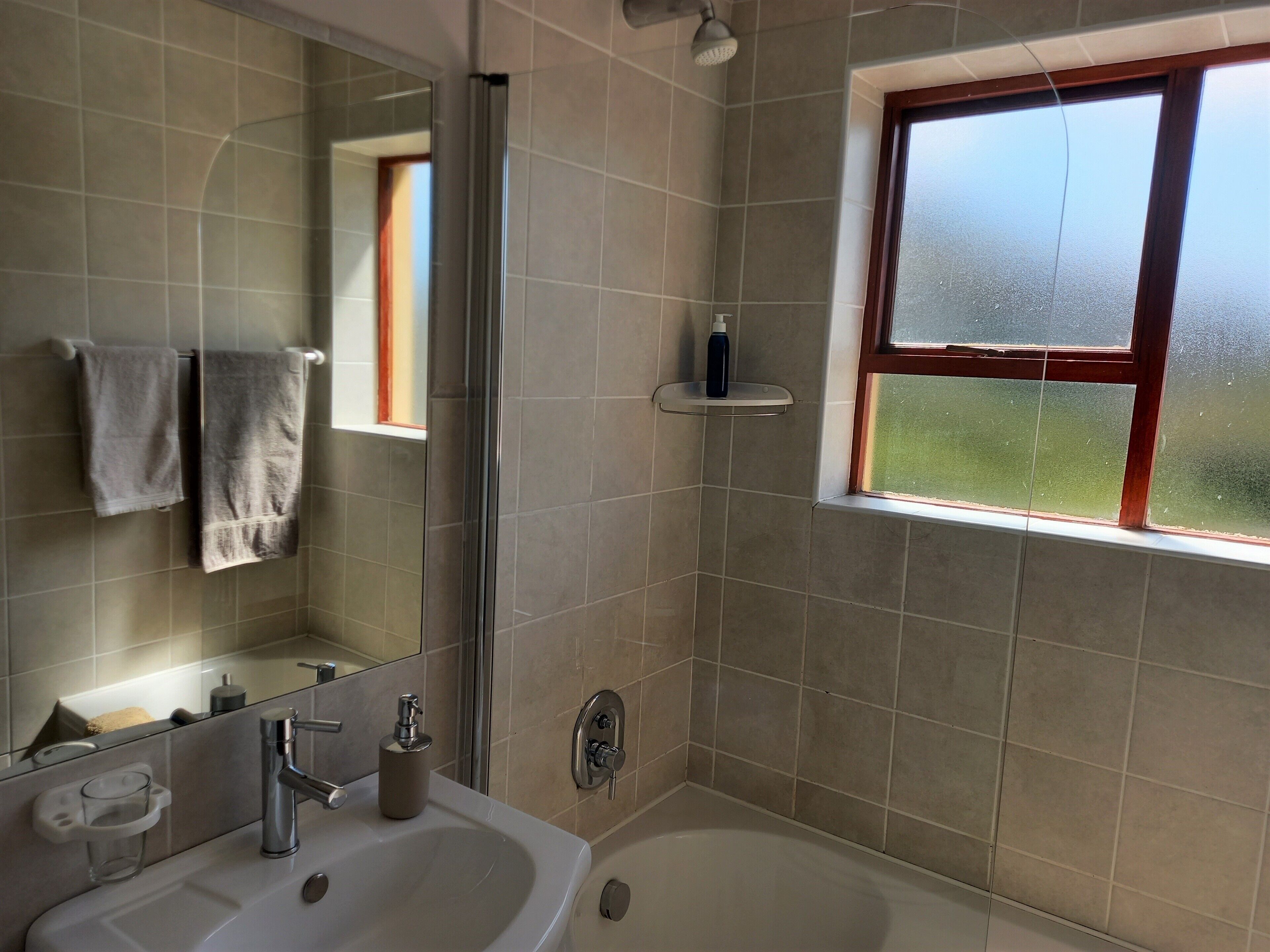 A bathroom with a bathtub, a sink, a mirror, a towel rack, and a window with a view of greenery.