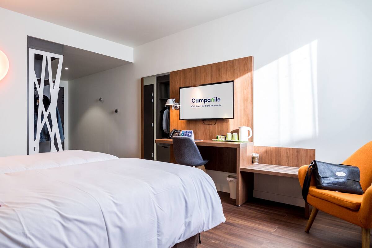 A hotel room with a bed, desk, chair, TV, and a coffee maker.