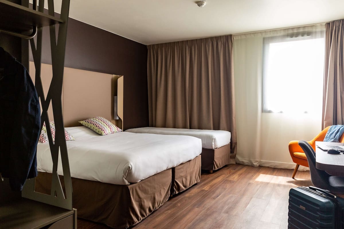 A hotel room with two beds, a desk with a chair, a suitcase, and a window with curtains.