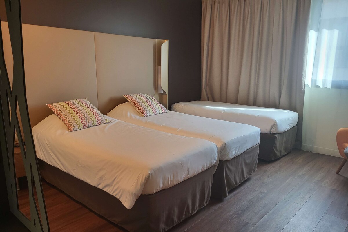 Een hotelkamer met twee bedden, een houten vloer en een raam met gordijnen.