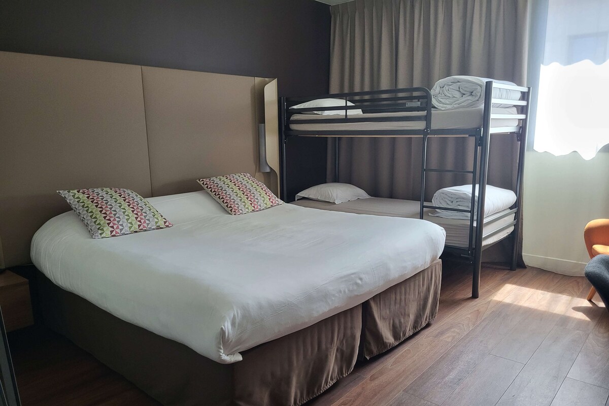 Een hotelkamer met een stapelbed, een groot bed met een gestreept kussen, en een houten vloer.