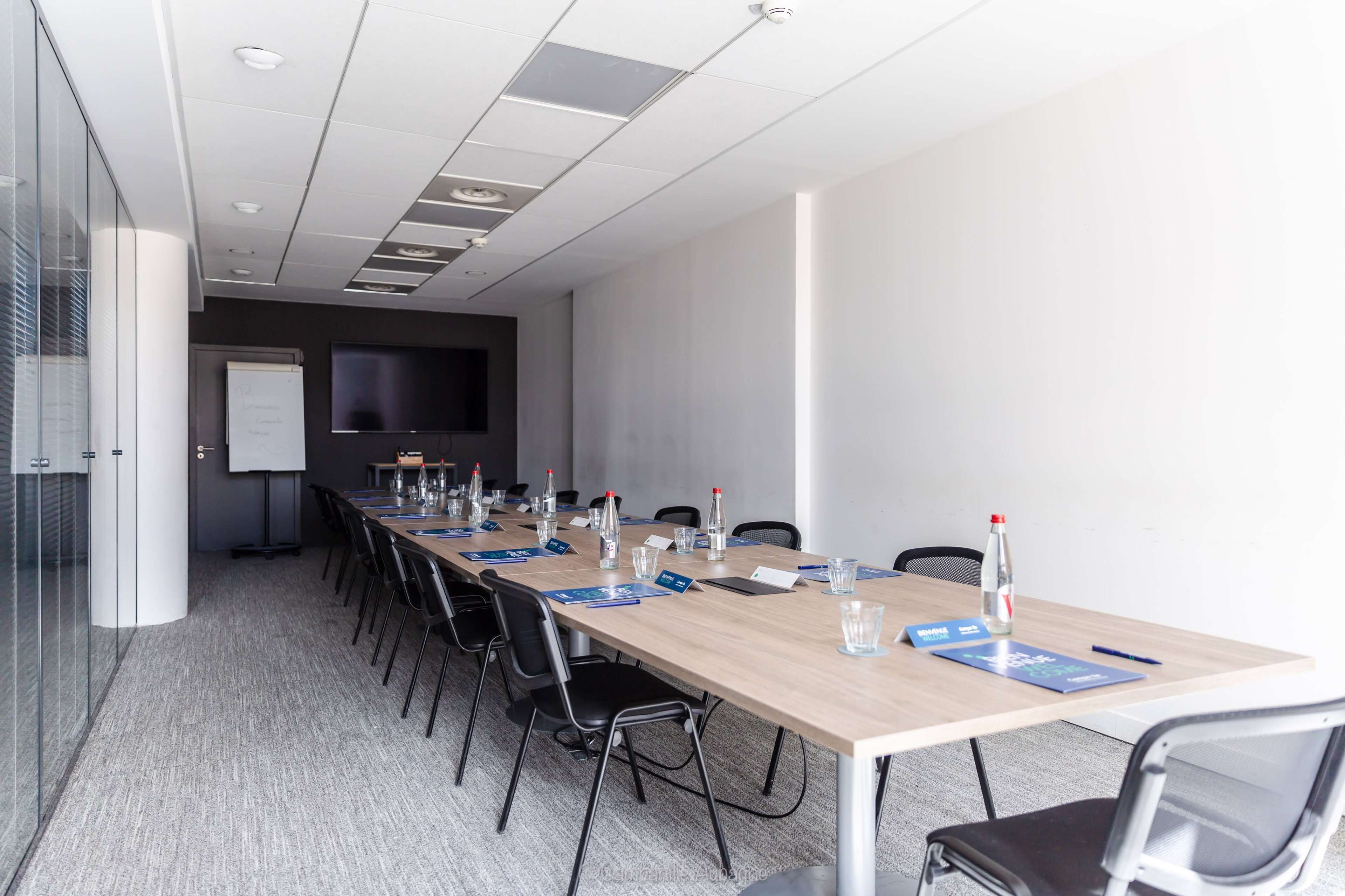 A conference room with a long table, chairs, a whiteboard, and a projector screen.