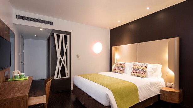 Een moderne hotelkamer met een groot bed, nachtkastjes, een bureau met stoelen en een televisie.