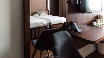 Une chambre d’hôtel avec deux lits, un bureau avec un téléphone et un téléviseur fixé au mur.