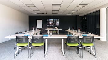 Un salón de conferencias con una mesa larga, sillas, una pizarra y una pantalla de televisión.