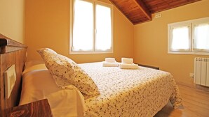A bedroom with a wooden ceiling, a large window, a bed with floral bedding, and a radiator. - Apartamentos Mont Romies Plaza (Naut Aran)
