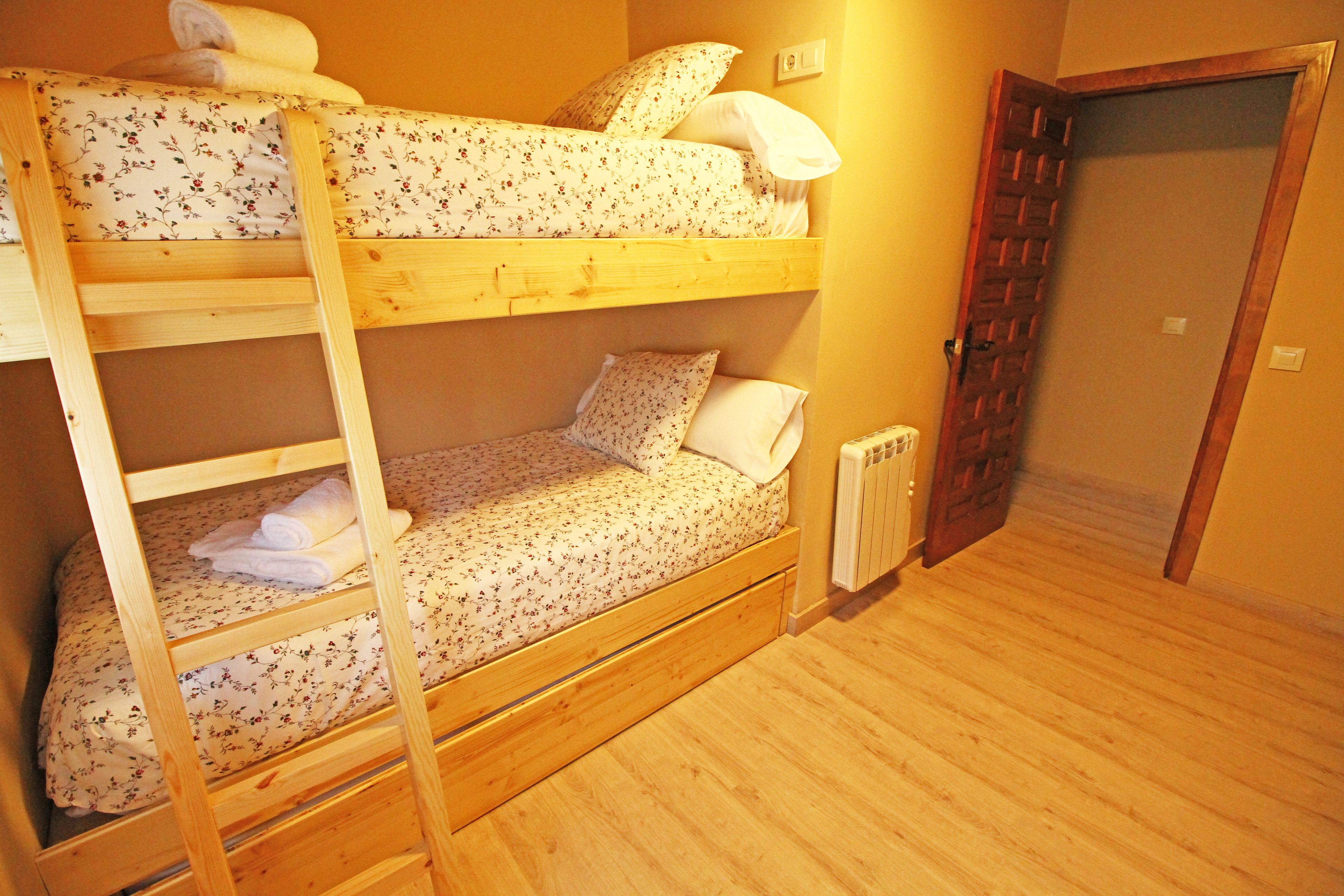 Une chambre avec des lits superposés, un plancher en bois et une porte située à droite.
