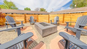 A patio area with Adirondack chairs, a concrete fire pit, and a wooden fence. - Minecart Motor Lodge (Montrose)