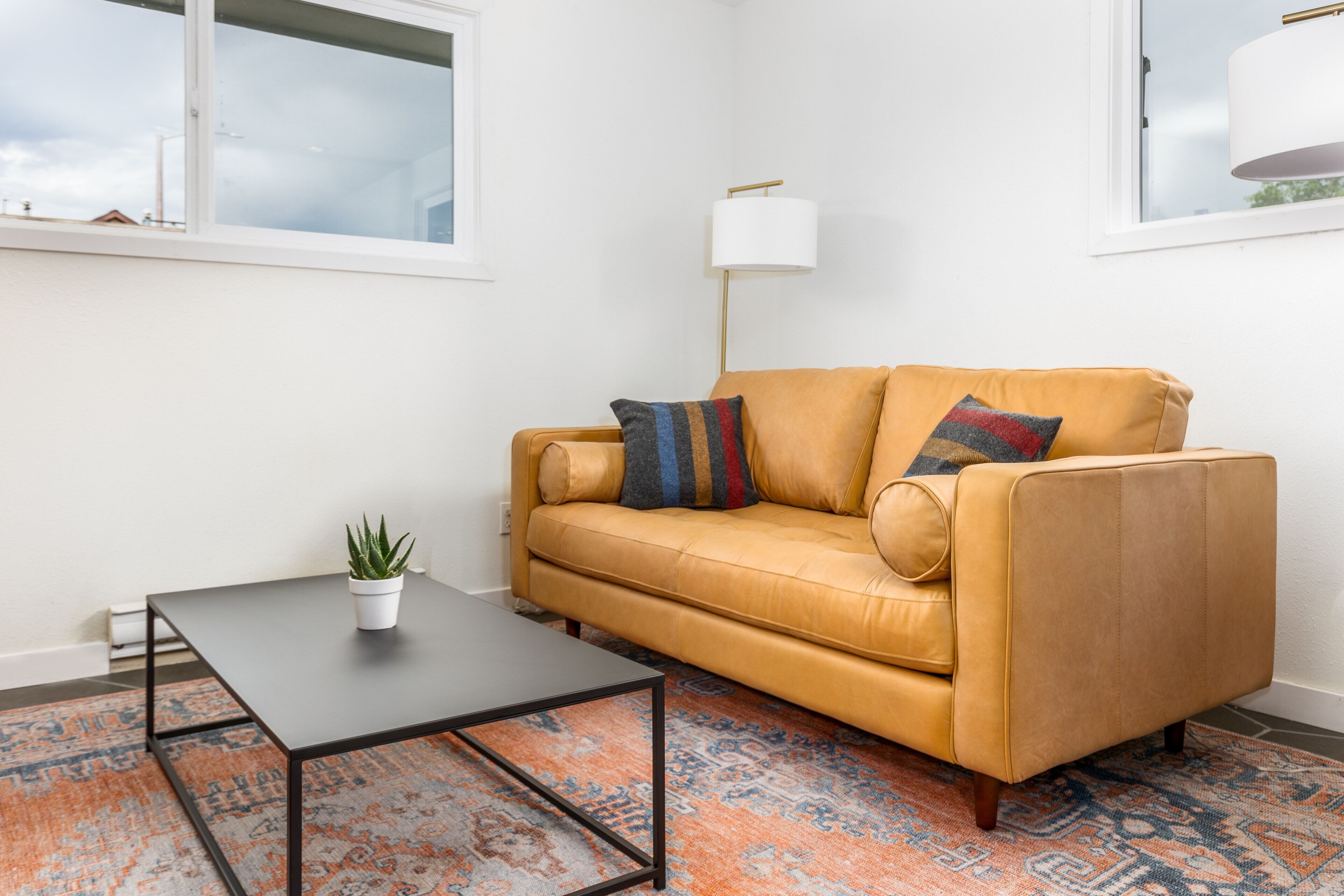 A living room with a yellow sofa, a small table, a floor lamp, and a patterned rug.