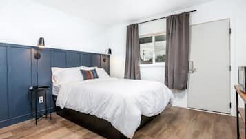 Un dormitorio moderno con cama, lámparas de noche, una mesita y una ventana con cortinas.