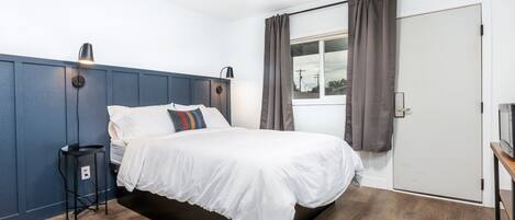 A modern bedroom with a bed, bedside lamps, a small table, and a window with curtains.