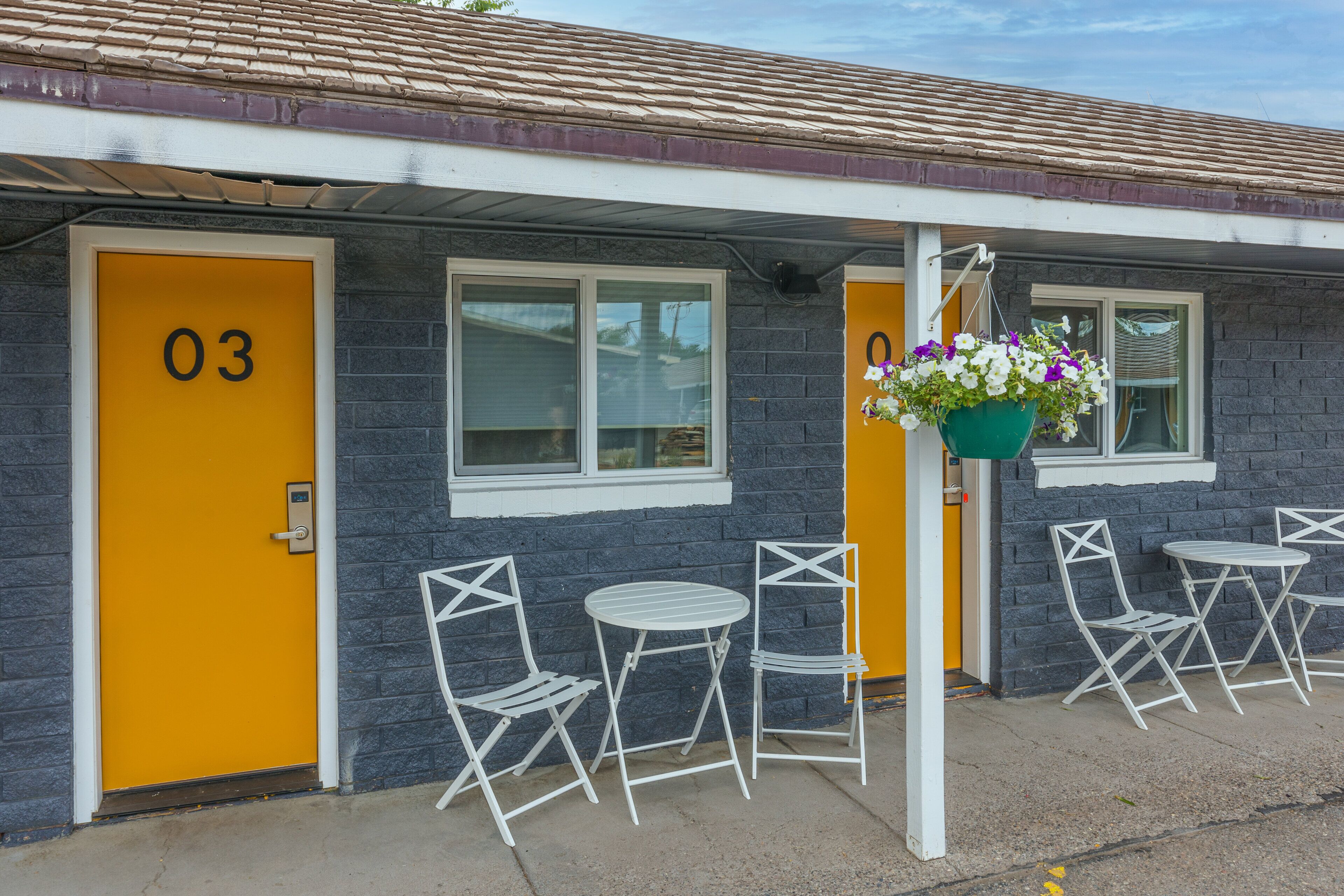 A motel with numbered doors, outdoor seating, and a hanging flower basket.