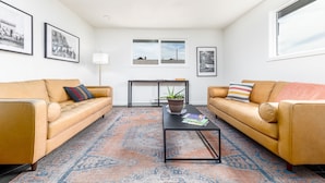 A living room with two leather sofas, a coffee table, a patterned rug, and framed pictures on the walls. - Minecart Motor Lodge (Montrose)